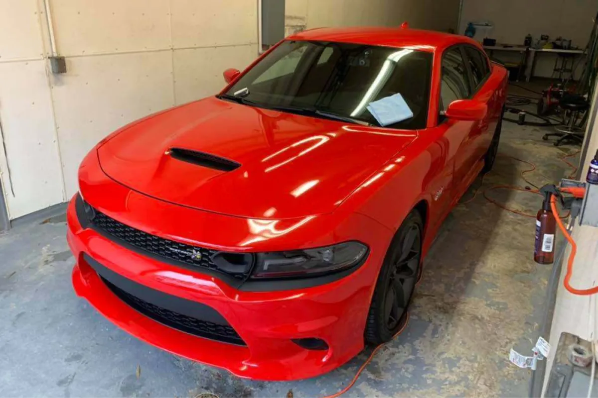 A red car in a garage with the hood scooped and the car's front visible.
