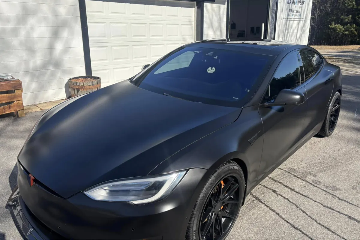 A car with a matte black wrap, showing side view and tinted windows.