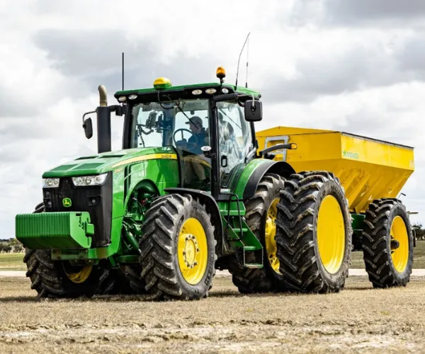 Green tractor with agricultural coating towing grain cart in field.