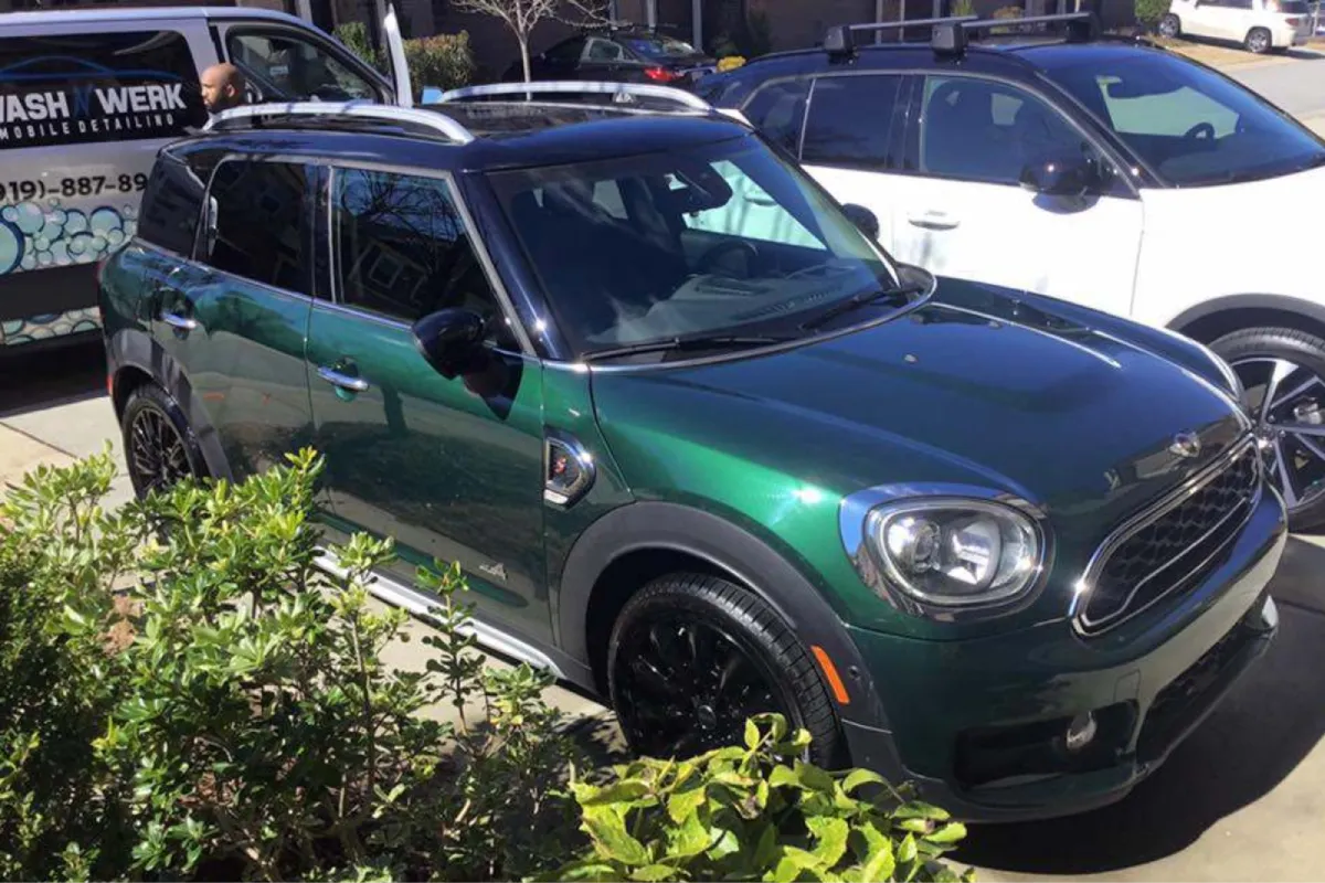 A green Mini Countryman SUV, with black accents and a sleek look, parked in a driveway.